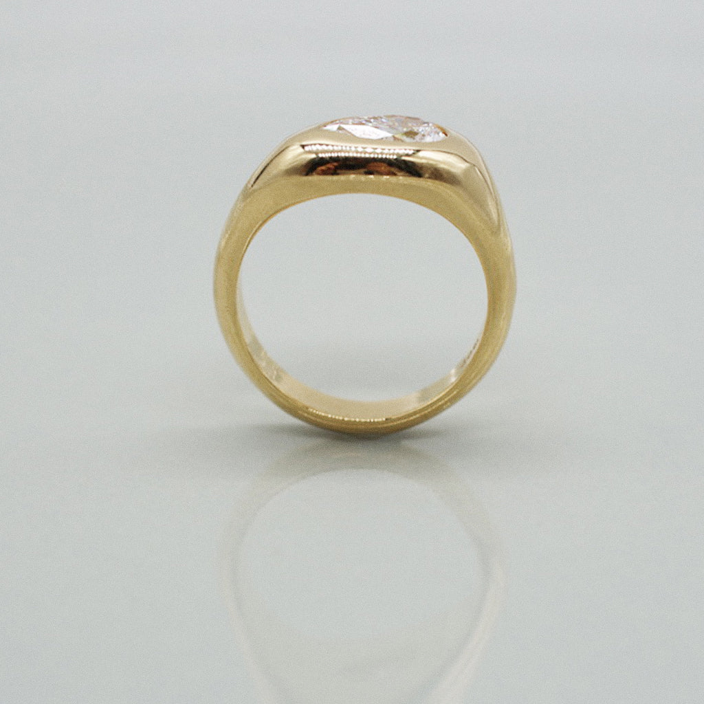 A yellow gold ring featuring a large pear cut diamond centre stone set against a clean white background with a soft reflection.