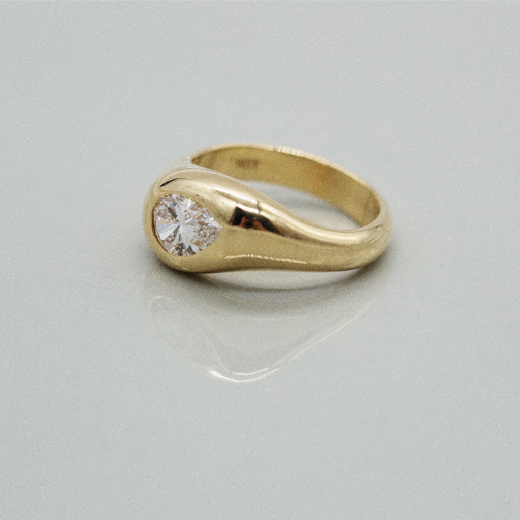 A yellow gold ring featuring a large pear cut diamond centre stone set against a clean white background with a soft reflection.