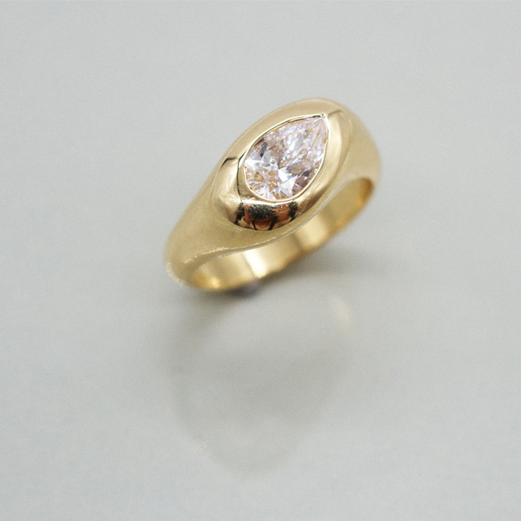 A yellow gold ring featuring a large pear cut diamond centre stone set against a clean white background with a soft reflection.