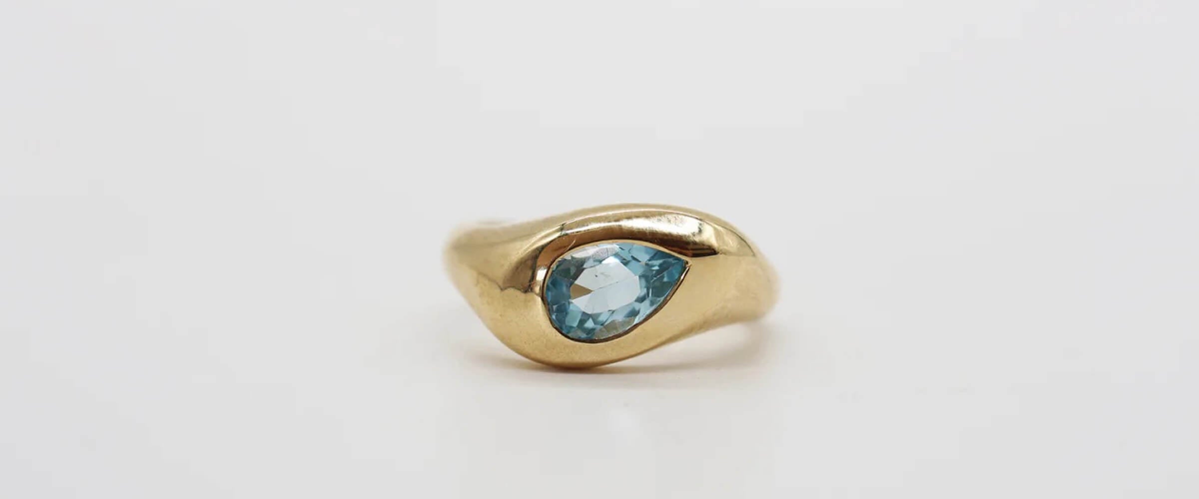 Gold ring with a blue gemstone on a light grey surface