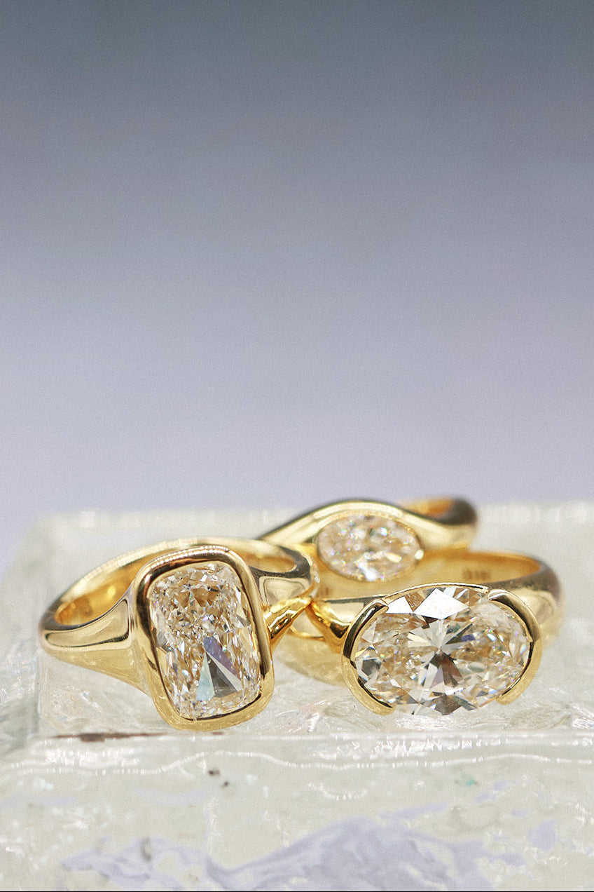 Three gold rings with diamonds displayed on a textured white surface against a soft gradient background.