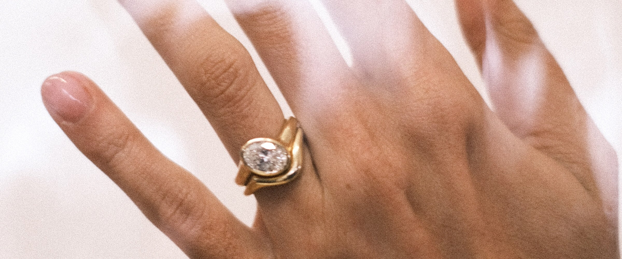 Gold ring with a diamond stacked with a plain gold band on a hand against a white background