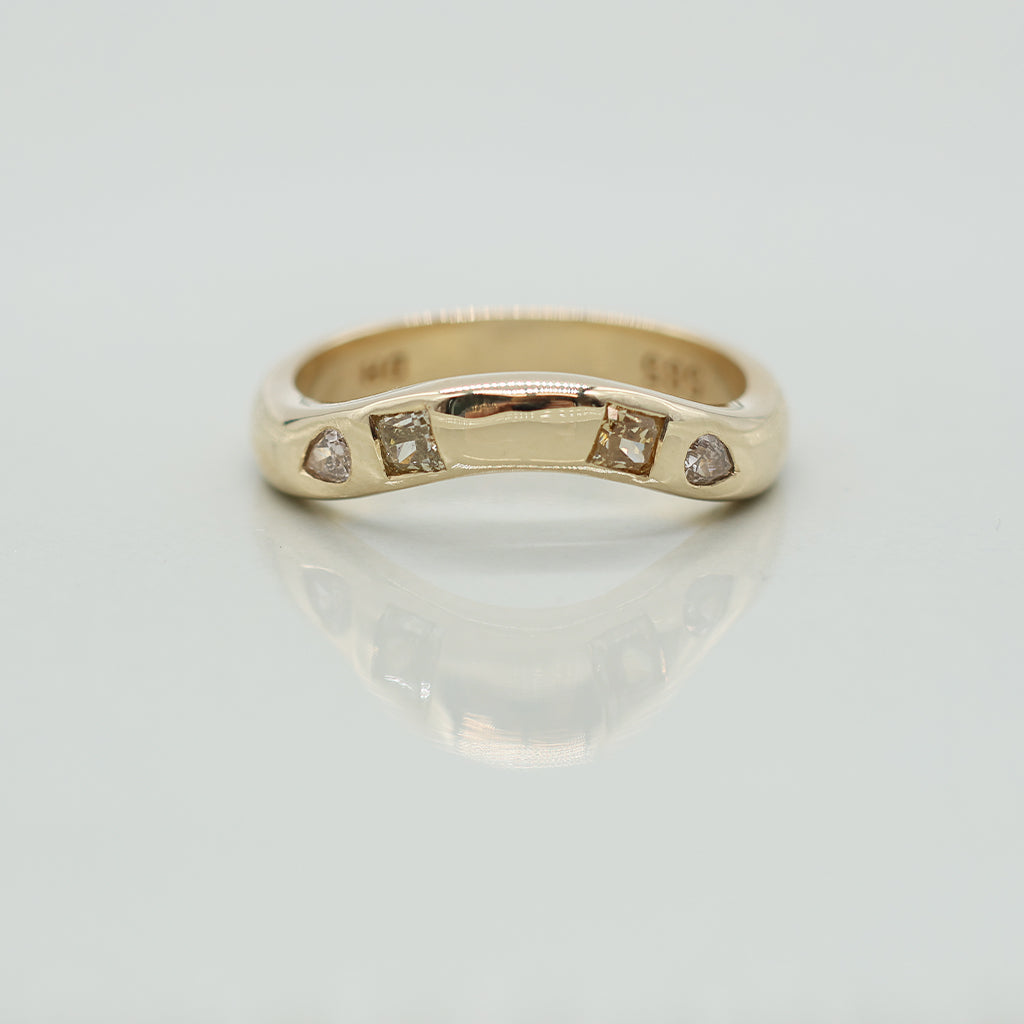 A yellow gold band ring featuring four small diamonds set in a row, photographed on a clean white reflective surface.