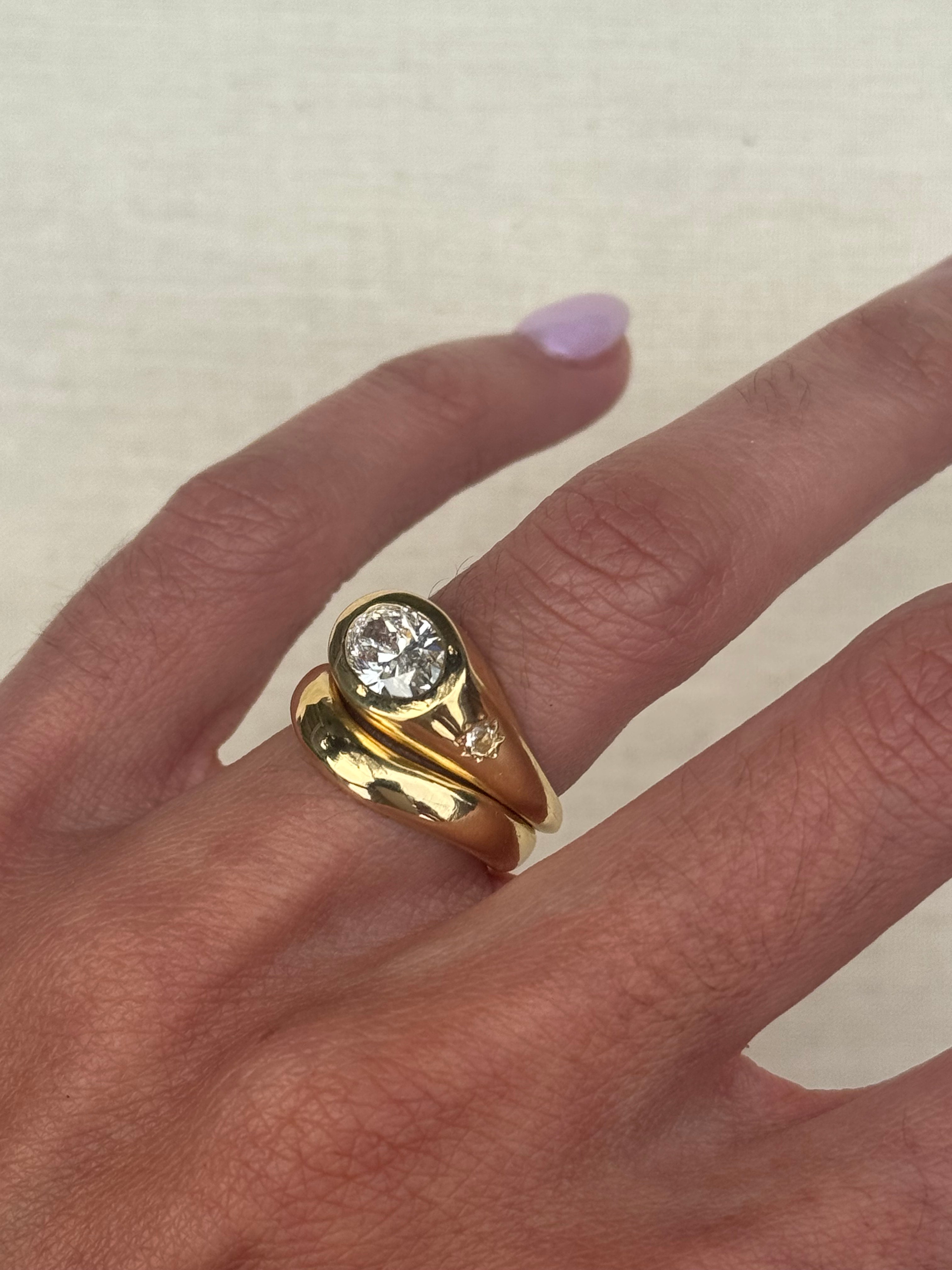 A yellow gold ring set featuring a large round brilliant-cut diamond on the main band and a smaller round diamond on a side post, photographed on the hand with neutral background.