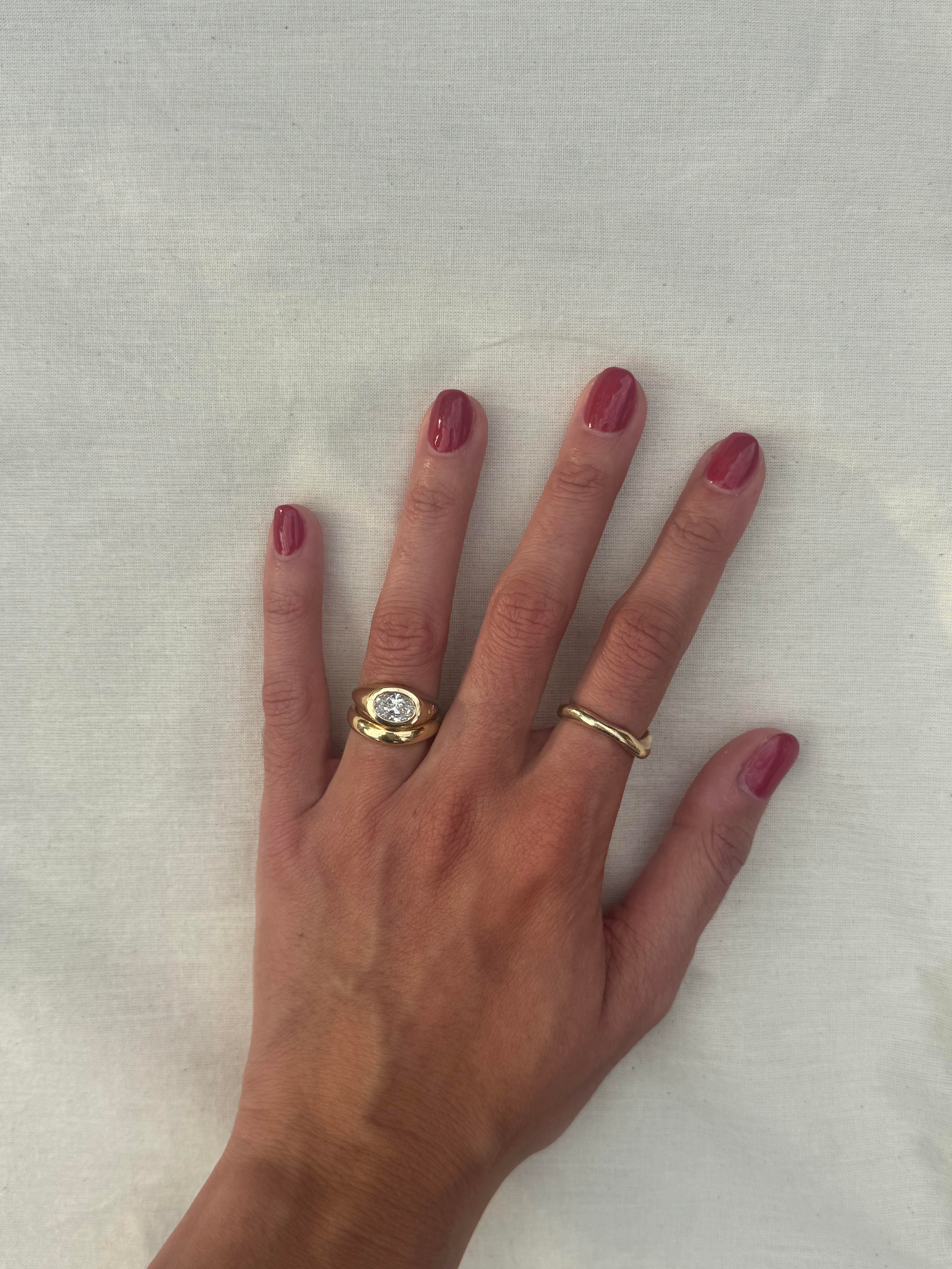 A yellow gold ring set featuring a large round brilliant-cut diamond on the main band and a smaller round diamond on a side post, photographed on the hand with neutral background.