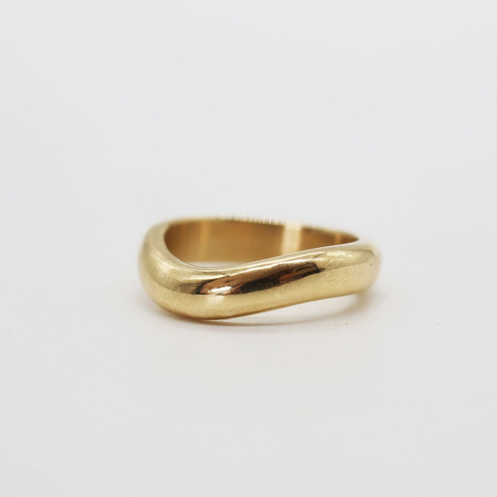 A polished yellow gold ring with a wavy, organic wavy band, photographed on a clean white background.