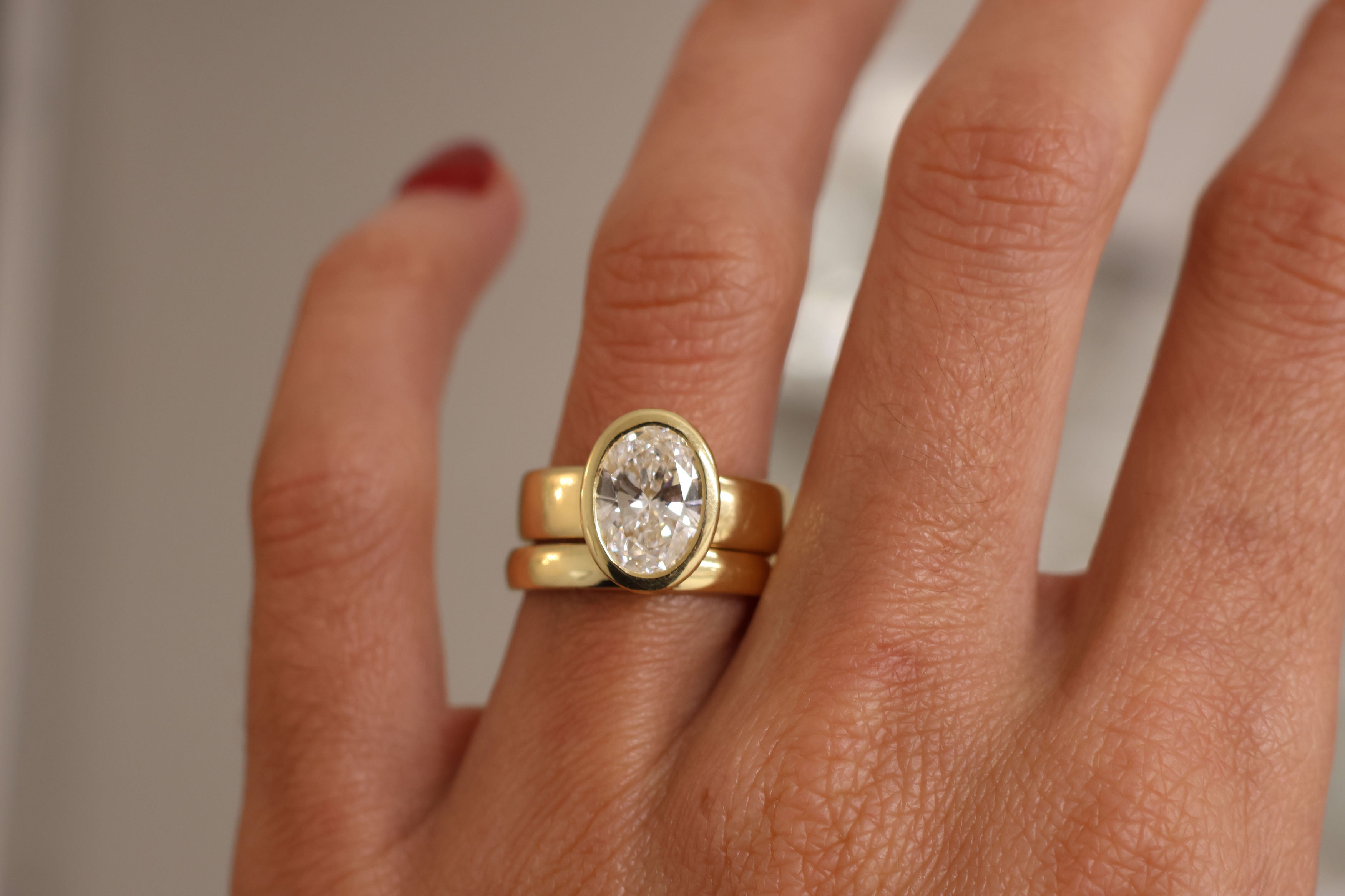 Gold ring with a diamond on a person's finger against a neutral background
