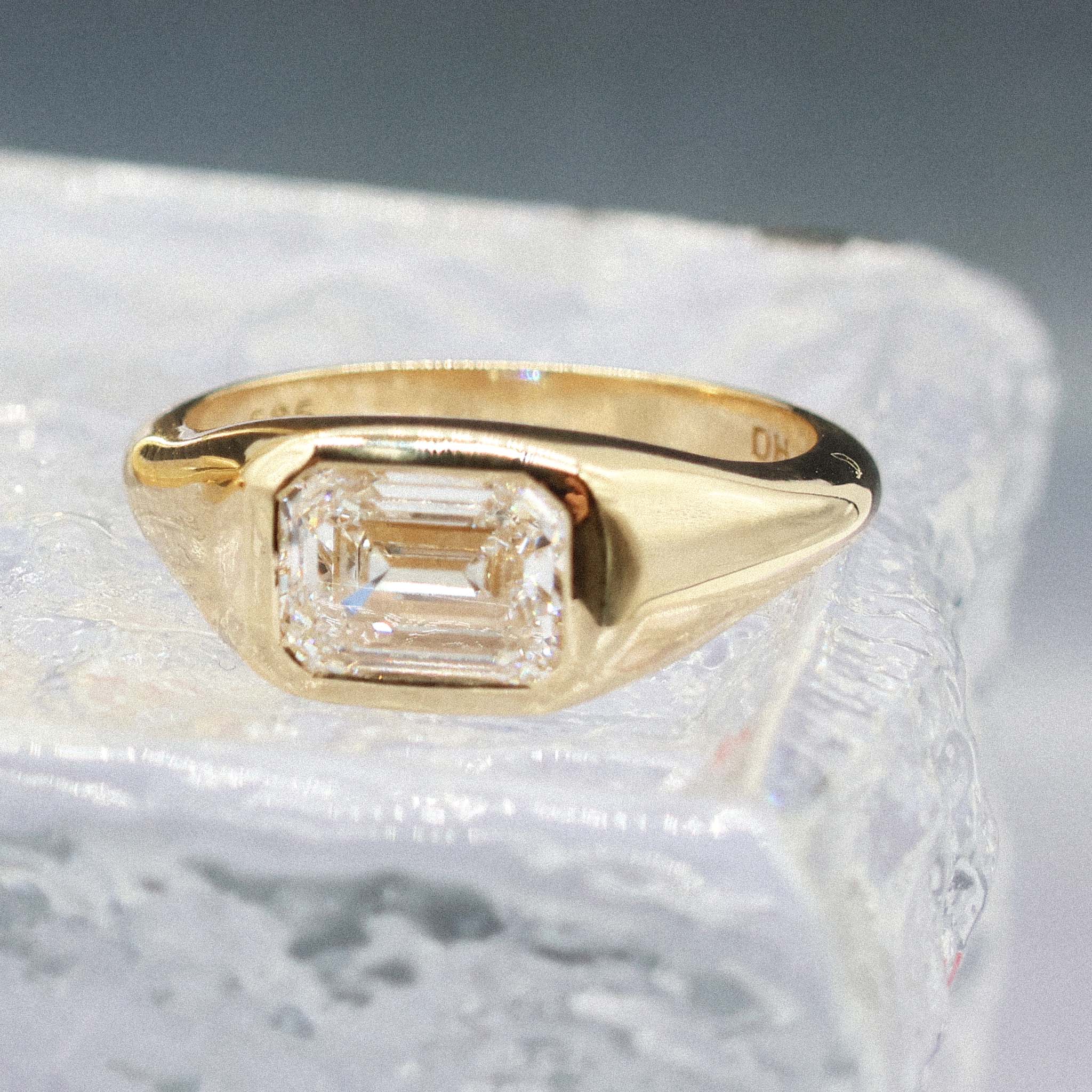 A yellow gold ring featuring a large rectangular emerald-cut clear gemstone, displayed on a textured white surface.