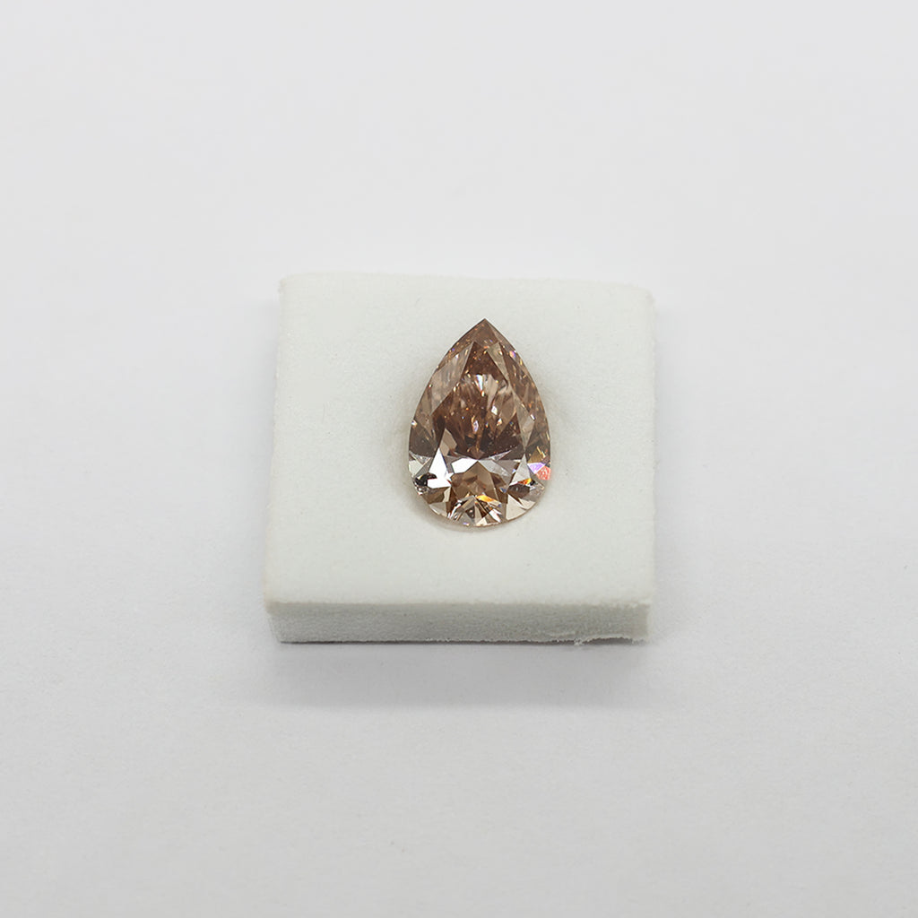 A single pear-cut peach-colored diamond displayed on a small white square cushion against a plain light background.